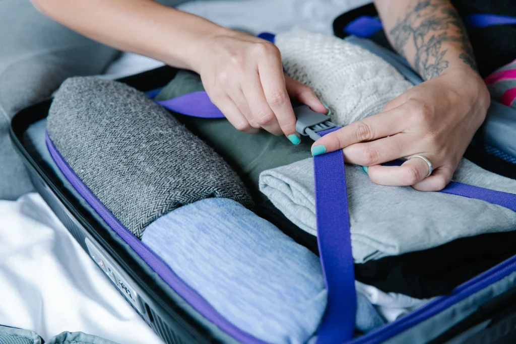 Hands securing folded clothes inside an open suitcase of someone after they learned how long rehab is and decided to go to Aloha Recovery California for 90 days.